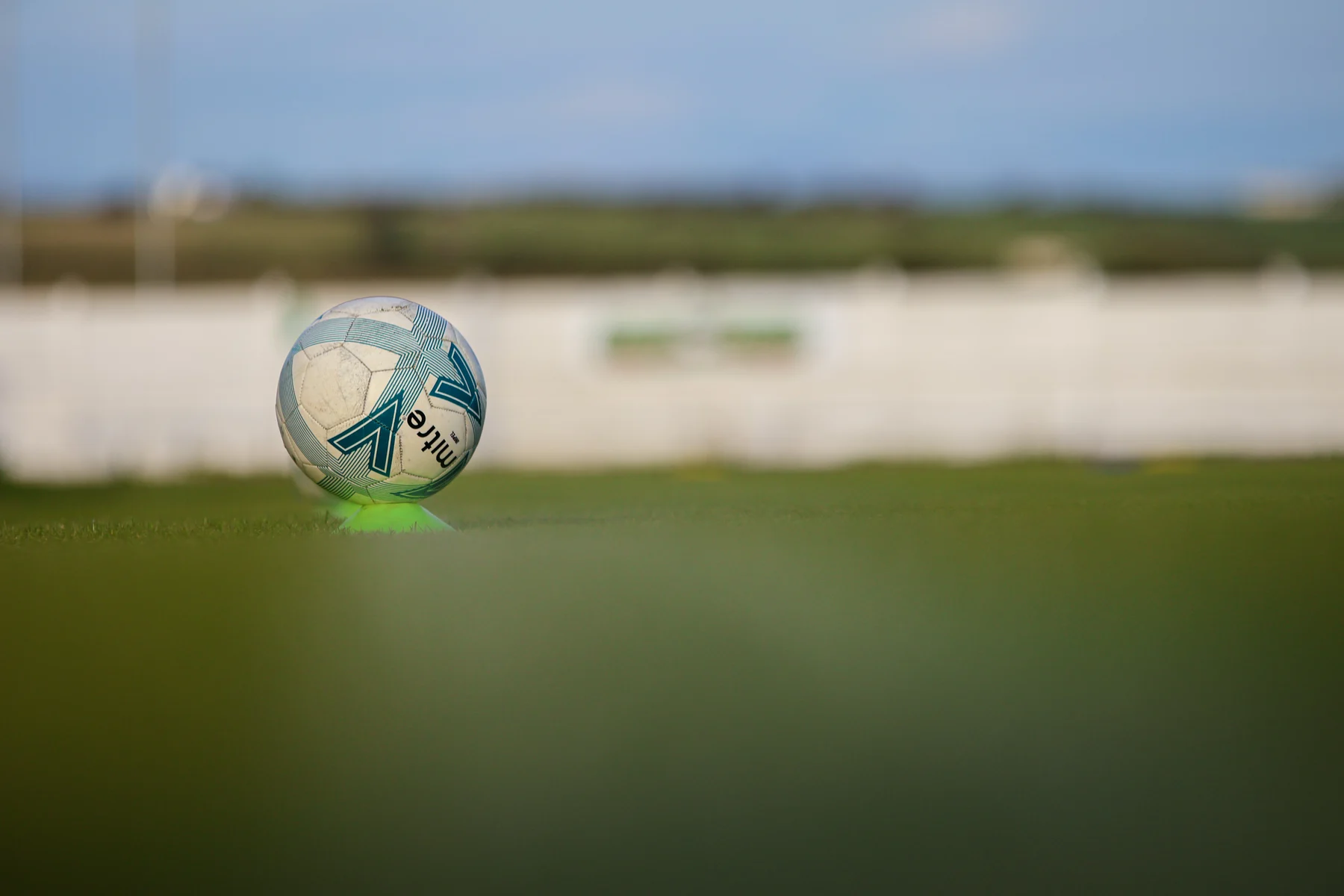 A football on a green training cone on a grass pitch